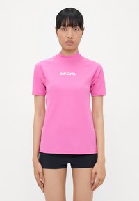 Short-sleeve, fitted pink rash guard made of stretchy material, featuring a high collar and white "RIP CURL" logo on the front.