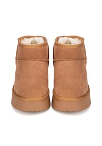Botas de ante marrón hasta el tobillo con un suave forro de piel blanca y suela de goma. Presentan detalles cosidos alrededor del tobillo.