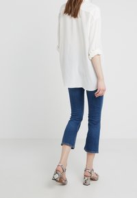 White, loose-fitting shirt with rolled sleeves, paired with blue, ankle-length flared jeans. Footwear features a snake print and chunky heel.
