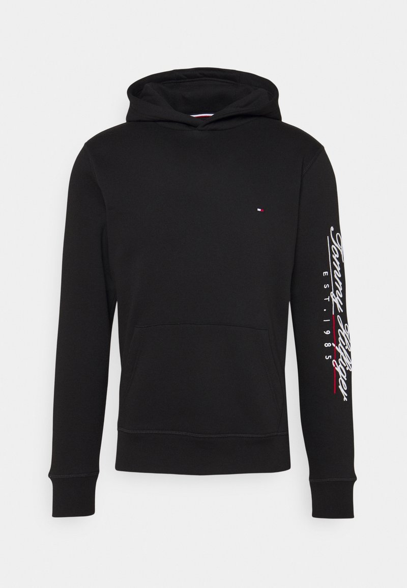 Sudadera negra de tejido suave con mangas largas, un bolsillo canguro y el logo "Tommy Hilfiger" impreso en blanco a lo largo de la manga izquierda.