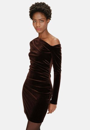 Robe en velours marron à manches longues, avec des détails froncés et un décolleté dénudé, présentant une coupe ajustée qui met en valeur la silhouette.