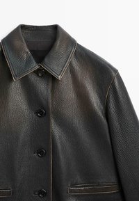 Giacca in pelle nera con finitura testurizzata, caratterizzata da un ampio colletto, cinque bottoni e cuciture a contrasto. Include due tasche laterali.