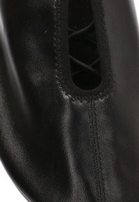 Zapato de cuero negro con una textura suave, presenta una abertura elástica y un sutil detalle de costura a lo largo del borde.