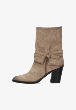 Bota de ante beige hasta el tobillo con un puño doblado, lazo decorativo y tacón grueso negro. Presenta una puntera puntiaguda y textura suave.