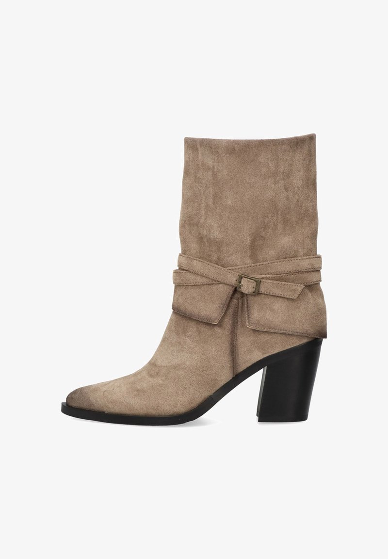 Bota de ante beige hasta el tobillo con un puño doblado, lazo decorativo y tacón grueso negro. Presenta una puntera puntiaguda y textura suave.