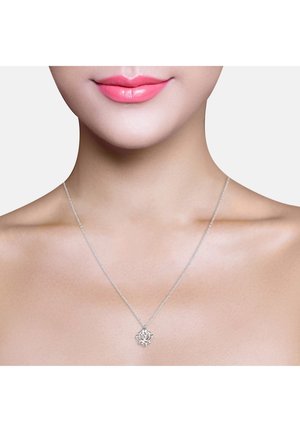 Gros plan d'une personne portant un délicat collier en argent avec un petit pendentif en forme de fleur de lotus sur une chaîne fine.