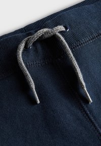 Marineblaues Joggingstoff mit geripptem Bund, ausgestattet mit einer grauen Kordel und metallenen Enden. Nahaufnahme von Nähten und Textur.