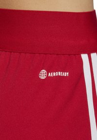 Rode sportieve shorts hebben een brede tailleband en witte strepen. De stof lijkt glad, met een prominent weergegeven logo met de tekst "AEROREADY".