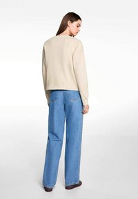 Beige Cropped-Sweatshirt mit Rundhals, der eine glatte Textur aufweist. Kombiniert mit lockeren blauen Jeans im klassischen Schnitt.