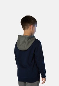Sudadera azul marino con capucha gris, hecha de tela suave. Presenta un bolsillo tipo canguro y puños elásticos, con costuras visibles.