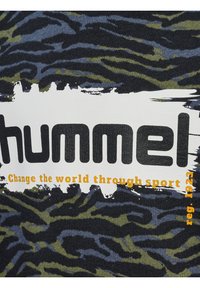 Svart och marinrandig tyg med gröna detaljer; har fet text "hummel" i svart och "Change the world through sport" i orange.