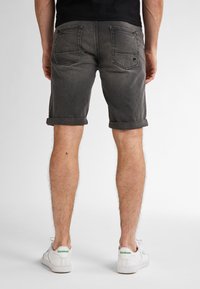Grijze denim shorts met opgerolde manchetten, voorzien van twee achterzakken en subtiele stikseldetails. Gadragen met witte Reebok sneakers.