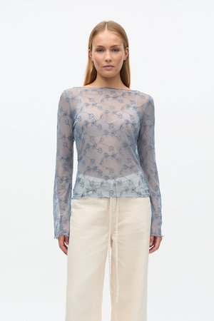 Haut bleu transparent à manches longues avec broderie florale, col rond et ourlet festonné, associé à un pantalon large couleur crème.
