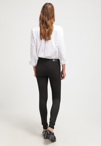 Černé skinny džíny vyrobené z elastického materiálu, s vysokým pasem, hladkou strukturou a minimalistickými zadními kapsami. V kombinaci s bílou košilí s knoflíky.