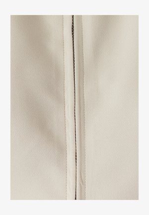 Beige Stoff mit glatter Textur, versehen mit einem zentralen Reißverschluss mit metallischen Details und verstärkten Nähten auf beiden Seiten.