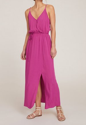 Femme portant une robe maxi sans manches magenta avec un col en V, une ceinture resserrée à la taille, une fente avant et des sandales plates beiges à brides.