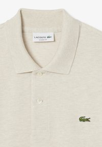 Beige pikétröja i mjukt tyg, med en klassisk passform, en två-knappsknäppning och en liten grön broderad krokodil-logotyp på vänster bröst.