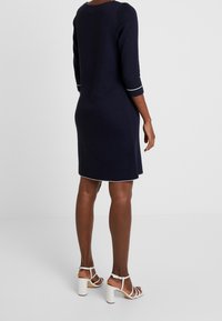 Robe en maille marine à manches trois-quarts avec bordures blanches aux manches et à l'ourlet. Associée à des sandales blanches à talon bloc, dévoilant une texture lisse.