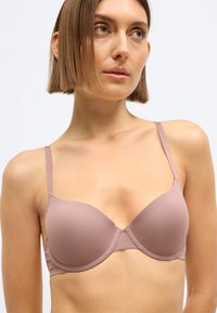 Svetlomalvová vystužená podprsenka s nastaviteľnými ramienkami, mäkká textúra, bezšvový dizajn a kostice pre podporu. Bez ozdôb alebo vzorov.
