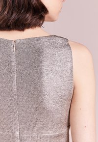 Metalická šedá bezramenná šaty s texturovanou tkaninou. Disponuje viditelným zadním zipem a čistými švy, které ukazují na přiléhavý střih.