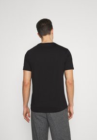 Camiseta negra de manga corta con cuello redondo, de textura suave, llevada al revés, combinada con pantalones grises con patrón.