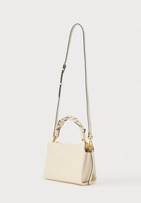 Borsa color crema con manico corto intrecciato e tracolla lunga regolabile con dettagli in metallo color oro, posata su uno sfondo bianco.