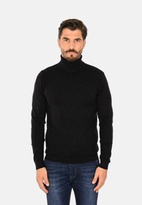 Maglione aderente nero a collo alto realizzato in morbido materiale, caratterizzato da una silhouette slim e orli e polsini a coste, abbinato a jeans blu.