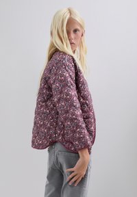Chaqueta acolchada en rosa con estampado de leopardo negro y púrpura, con escote redondeado y acentos grises. Combinada con jeans grises.