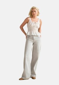 Lehký bílý peplum top s předním šňůrkovým stahováním a elastickým pasem, kombinovaný s širokými světle šedými džíny a béžovými tkanými muly.