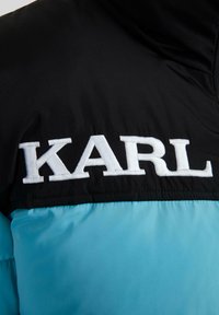 Giacca imbottita con una parte superiore nera e una parte inferiore azzurra chiara. La parola "KARL" è ricamata in bianco sul tessuto nero.
