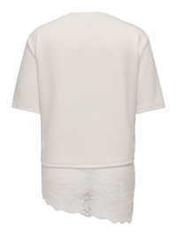 Haut blanc à manches courtes avec un ourlet asymétrique comprenant une superposition de dentelle plus longue d'un côté à l'arrière.
