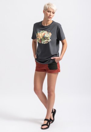 T-shirt gris avec un graphique floral coloré, assorti à un short couleur rouille avec des accents noirs. Le modèle porte des sandales noires.