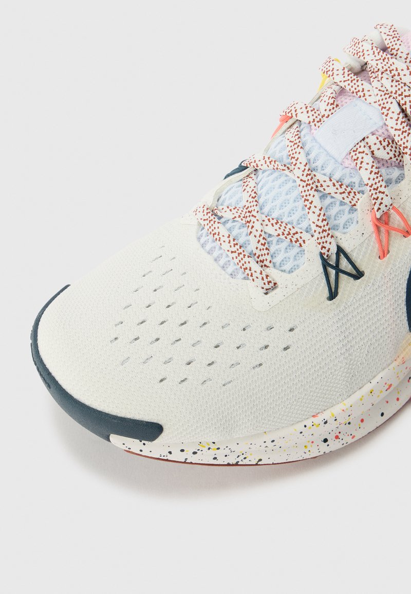 Białe buty sportowe z siateczkową cholewką, teksturowanym wykończeniem z tkaniny, wielokolorowym, nakrapianym śródpodeszwą oraz kontrastującym, ciemnoniebieskim akcentem na palcu.