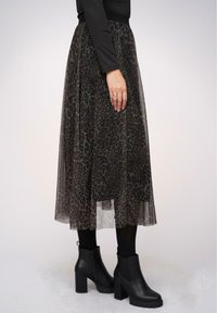 Gonna lunga nera in tulle con motivo a stampa leopardata. Abbinata a stivali neri alla caviglia e indossata su collant neri. Vita semplice.