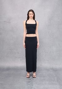 Conjunto de dos piezas negro de canalé que consiste en un top corto ajustado con escote cuadrado y una falda maxi larga y recta. Se llevan sandaliasplanas.