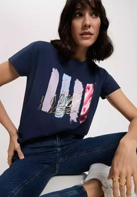 Granatowy T-shirt z graficznym nadrukiem, który przedstawia wzory pędzla w pastelowych kolorach oraz kwiatowy motyw z złotymi akcentami.