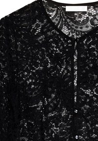 Black lace cardigan featuring a floral pattern, round neckline, and button closure with small, shiny buttons. Lightweight and textured fabric.