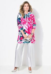 Barevná květinová mikina v růžové, bílé a tyrkysové barvě, kombinovaná s lesklými stříbrnými kalhotami s širokými nohavicemi. Mezi výrazné prvky patří kapuce se stahovací šňůrkou a lesklé akcenty.