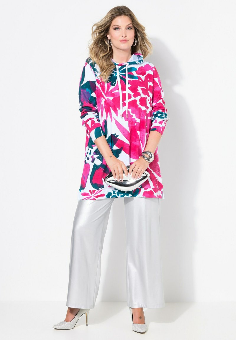 Barevná květinová mikina v růžové, bílé a tyrkysové barvě, kombinovaná s lesklými stříbrnými kalhotami s širokými nohavicemi. Mezi výrazné prvky patří kapuce se stahovací šňůrkou a lesklé akcenty.