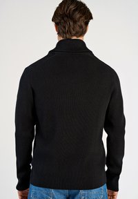 Zwarte geribbelde gebreide trui met een hoge kraag en lange mouwen. Het ontwerp beschikt over een gestructureerd oppervlak en een getailleerde silhouette.