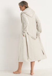 Ljust grå badrock i mjukt fleece-material, med huva, framfickor och ett knytbälte. Knälång med sidoöppningar för extra komfort.