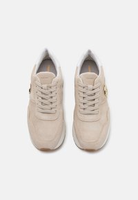 Baskets en suédine beige avec un bout rond, présentant un laçage à l'avant, un col rembourré et un accent logo doré sur le côté.