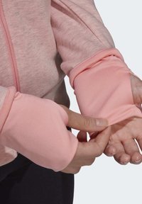 Mains ajustant le trou du pouce d'un haut de sport rose à manches longues avec poignets pour le pouce sur un fond uni.