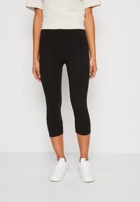 Fekete, bokáig érő leggings rugalmas anyagból, testhezálló fazonnal, fehér sportcipővel párosítva a teljes öltözékhez.