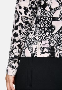 Black and white patterned long-sleeve sports top with various graphic designs. Includes a Marc Cain Sports label at the hem.