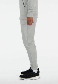 Hellgraue Jogginghosen aus weichem Stoff, mit einer schmalen Passform und dezentem Branding. Kombiniert mit schwarzen Sportschuhen und weißen Socken.