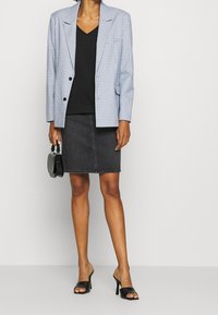 Blazer bleu à carreaux, haut noir à encolure en V, jupe en denim grise, talons ouverts noirs, tenant un petit sac à main noir. Coupe standard et design ajusté.