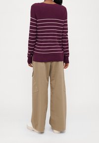 Mörkröd stickad tröja med vita horisontella ränder, rund halsringning, långt ärm och avslappnad passform; kombinerad med beige cargobyxor och vita skor.