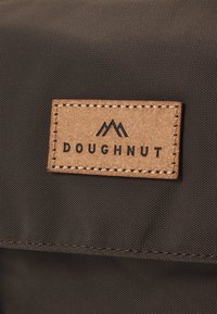 Brown fabric with a textured surface features a rectangular leather tag embossed with "DOUGHNUT" and mountain logo, stitched with light thread.
