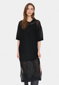 Rochie din plasă neagră cu mâneci scurte, având un sistem de închidere cu butoni, fante laterale și un design texturat. Ușoară, cu croi lejer.